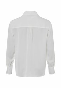 Blusa bianca a maniche lunghe con dettaglio a yoke sul retro, tessuto morbido, orlo arrotondato e maniche arricciate ai polsini per una vestibilità strutturata.