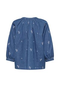 Blouse bleue à manches longues avec un col froncé et une petite broderie florale blanche dispersée sur le tissu.