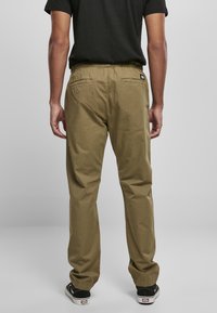 Pantalones khaki con cintura elástica, dos bolsillos traseros y un diseño de pierna recta. Combinados con zapatos negros con suelas blancas.
