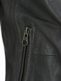 Svart läderjacka med närbild av en metall YKK dragkedja och sömnadsdetaljer. Texturerad yta med en stilren design.