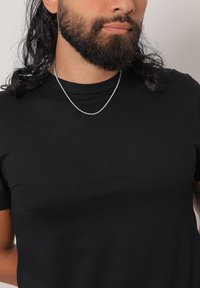 Schwarzes T-Shirt mit kurzen Ärmeln und glatter Textur, mit einer silbernen Kette, die auf dem Schlüsselbein liegt.