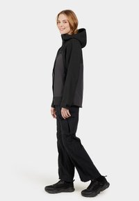 Black and gray waterproof jacket with a hood, featuring zippered pockets and a relaxed fit, paired with black cargo pants and sneakers.