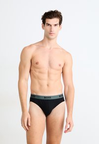 Boxers noirs pour hommes avec une ceinture verte arborant le logo "BOSS". Le tissu est extensible et ajusté, conçu pour le confort et le soutien.