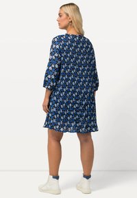 Sininen kuvioitu mekko 3/4 hihoilla ja kirjavalla hameella, jossa on kukkakuvio erilaisissa sinisen ja valkoisen sävyissä, valmistettu kevyestä kankaasta.