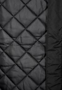 Černá prošívaná tkanina s diamantovými vzory. Hladký povrch s matným finišem. Obsahuje jednobarevný černý okraj na jedné straně.