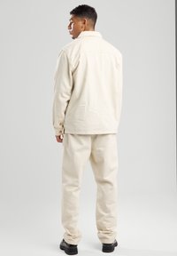 Licht crèmekleurige jas met een kraagontwerp, voorzien van knoopaccenten; gecombineerd met bijpassende broeken en zwarte laarzen.