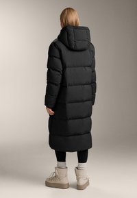 Fekete steppelt télikabát kapucnival, hosszú fazonú, sima tapintású. Bézs téli csizmával és fekete leggingsszel kiegészítve.