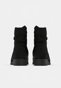 Mustad mustad saapad, millel on pehme ja longus ülemine osa, madal konts ja tagaküljel lukk lihtsaks panekuks.