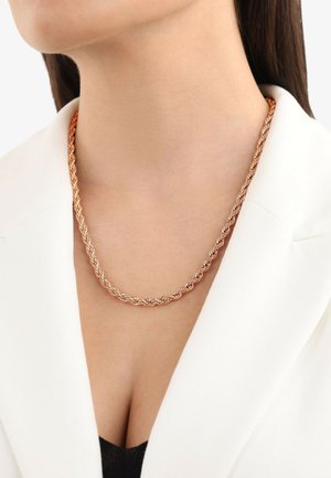 Twisted metalen ketting met een mix van roségouden en zilveren tinten, gedragen over een zwarte top en een witte blazer.