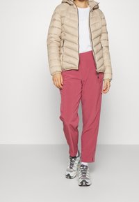 Beige polstret jakke med hætte, hvid t-shirt og lyserøde loose-fit bukser. Stylet med multicolore sportsko.