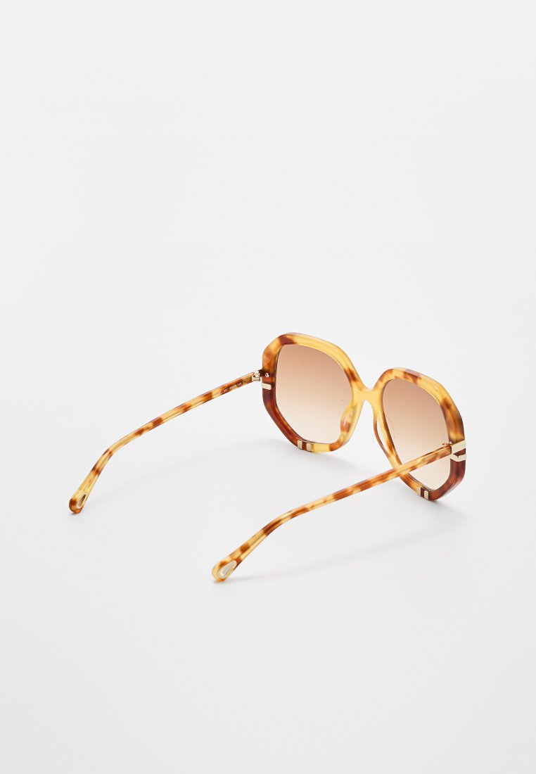Achtkantige Sonnenbrille mit einem hellbraunen Schildpatt-Rahmen und einem braunen Verlaufsglas. Hat dünne, gemusterte Bügel.