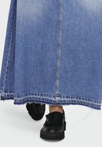 Jeanskjol i ljusblått med fransade kanter, tillsammans med svarta plattformsskor med volangdetalj och platt sula.