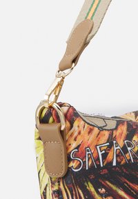 Kangas laukku, jossa on värikäs safari-kuosi. Mukana on sileä, vaalea nahkaremmi, jossa on kullanvärinen solki ja korostukset.