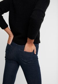 Mörkblå denimjeans med en figursydd design, försedda med bakfickor och en slät yta, i kombination med en svart, fluffig tröja.