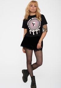 Black cropped t-shirt with a circular graphic design in white and pink, paired with black velvet shorts featuring lace trim. Black boots.