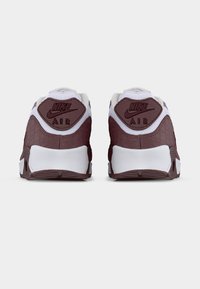 Ζευγάρι λευκά και μαρον Nike Air sneakers, φωτογραφημένα από πίσω, με υφή στην επάνω επιφάνεια και λογότυπο στις ταμπέλες της φτέρνας, πάνω σε απλό φόντο.