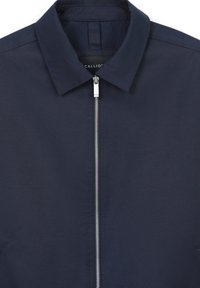 Giacca blu navy con zip frontale, colletto a ribalto e tessuto liscio. Presenta una zip argentata e un'etichetta del marchio discreta all'altezza del collo.