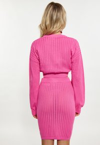 Completo in maglia rosa aderente con texture a coste verticali, maniche lunghe e una vita. Il vestito termina a metà coscia e presenta una silhouette aderente.