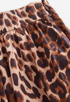 Tyg med leopardmönster som har nyanser av brunt och svart med en veckad struktur längs den övre kanten, som visar mjukt och lätt material.