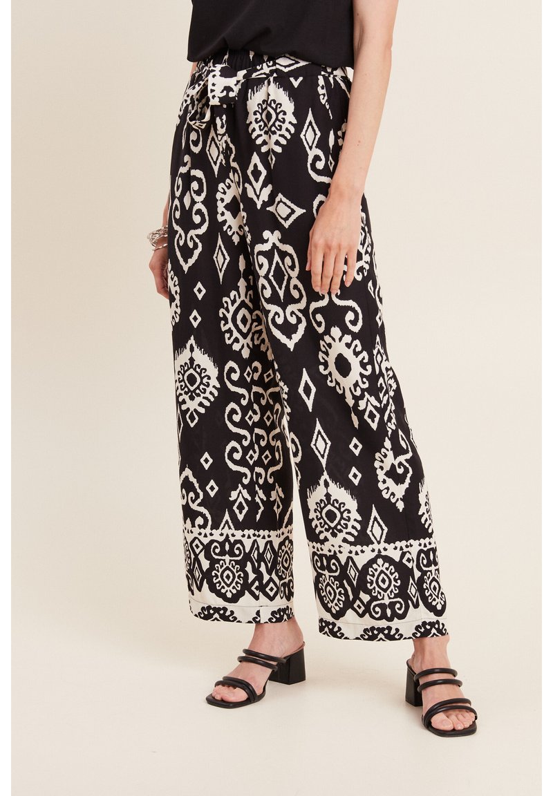 Zwart-witte, gestreepte wijde broek met een trekkoord in de taille en decoratieve accenten, gecombineerd met zwarte sandalen met blokhak.