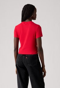 T-shirt rouge à manches courtes en côtelé avec un col ras du cou, associé à un jean en denim noir taille haute avec poches arrière et étiquette logo Levi's.