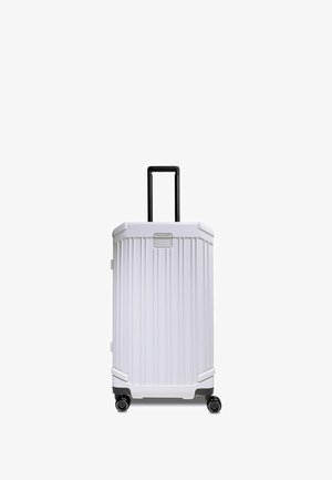 Weißer Hartschalenkoffer mit vertikal geriffeltem Design, schwarzem Teleskopgriff, vier drehbaren Rollen und grauen Akzenten am Boden.