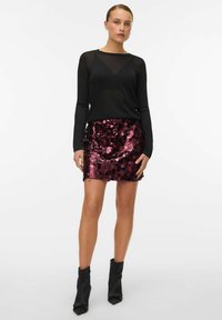 Czarna bluzka z długim rękawem z przezroczystym fragmentem, zestawiona z obcisłą, cekinową bordową spódnicą. Stylizację uzupełniają czarne botki za kostkę.
