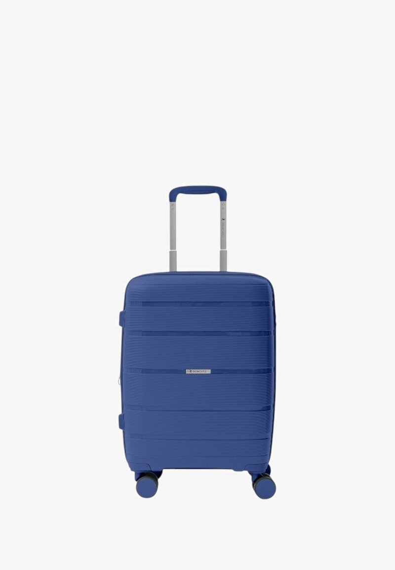 Valigia rigida blu con linee orizzontali texturizzate, manico telescopico, quattro ruote e una placca con logo argentato sulla parte frontale.