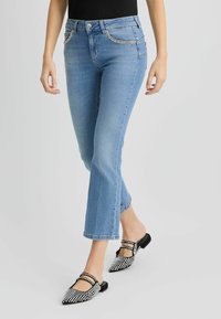 Jeans en denim bleu clair avec une coupe ajustée, taille mi-haute et deux poches avant. Détail de bord argenté remarquable sur les bords des poches.