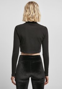Sort cropped langærmet top lavet af glat stof, parret med højtaljede sorte fløjlsleggings med en blød glans.