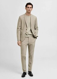 Costume beige clair ajusté avec un pull assorti, comprenant un blazer structuré, un pantalon slim et des chaussures en cuir noires. Texture de tissu lisse.