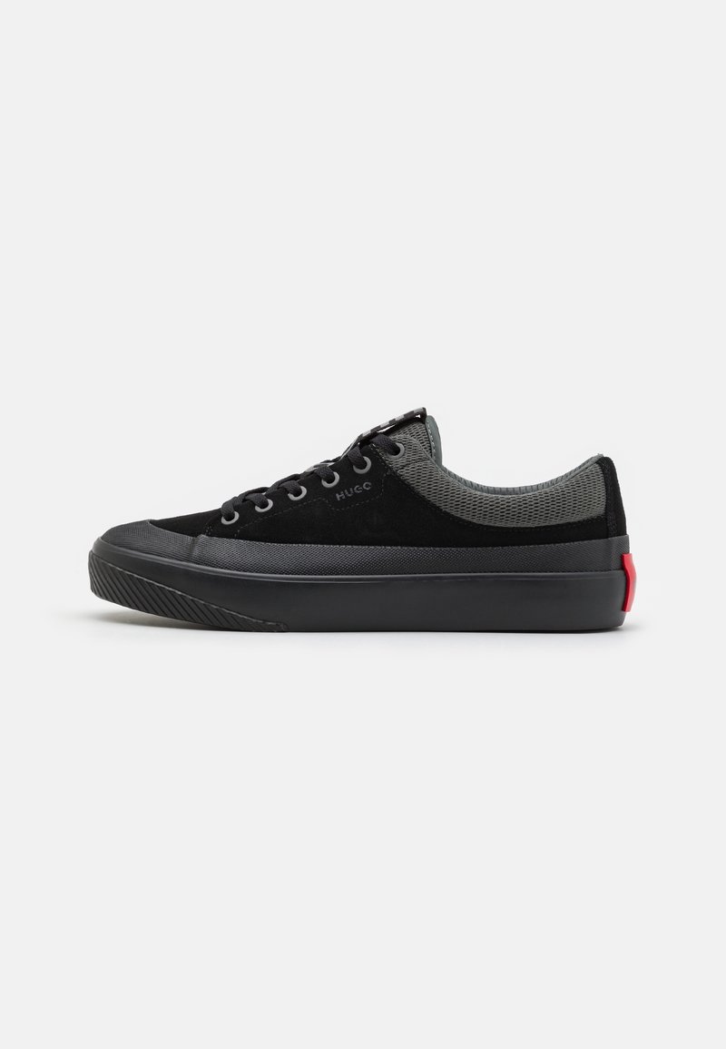 Zapatillas negras y grises con parte superior de ante, acentos de malla, cordones redondos, suela de goma y un distintivo acento en el talón rojo.
