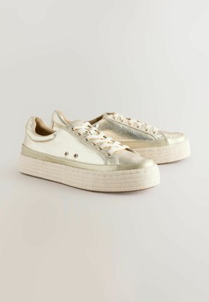 Zapatillas plataforma con un upper en dorado metálico y blanco, detalles texturizados y suela de cuerda trenzada. Cordones y ojales en tonos a juego.