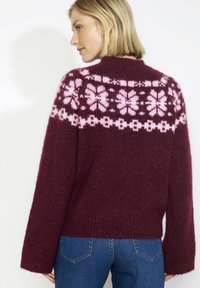 Bordový sveter s ružovými geometrickými vzormi na priekrčníku, rebrovanými manžetami a lemom. Mäkká, nadýchaná textúra, voľný strih.