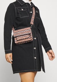 Borsa a tracolla con motivo intrecciato in rosa e nero, forma rettangolare con chiusura a pattina, tracolla regolabile e accentuazioni metalliche.