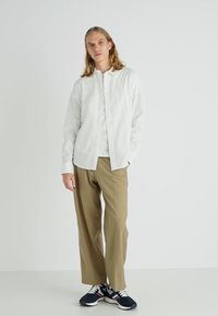 Chemise blanche à manches longues avec boutons, pantalon beige à jambes larges et baskets noires. Design minimal, coupe décontractée et texture en coton.