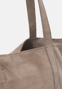 Sac fourre-tout en daim taupe clair avec deux anses cousues, gros plan montrant la texture et les détails de la couture.