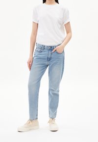 Světlé modré džíny s vysokým pasem, zúženými nohavicemi a klasickým designem s pěti kapsami, spárované s bílým tričkem s krátkým rukávem z bavlny a béžovými teniskami.