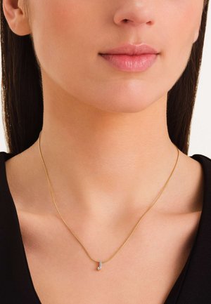 Gouden ketting met een dunne schakel en een gebogen hanger versierd met kleine heldere steentjes, rustend op een gladde nek.