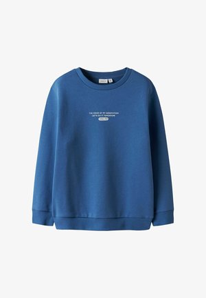 Sinine ümarselgusega dressipluus soonikkoes mansettide ja äärega, esiküljel valge tekst "MINU PÕLVKONNA HÄÄL TEEME SEDA HOMME ALATES 1986".