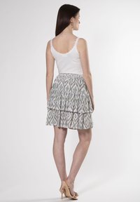 Weißes Top mit Spitzenrand, geschichteten grauen und grünen gemusterten Rock, beige hochhackige Sandalen, von hinten gesehen.