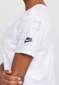 Vit Nike Air t-shirt med andningsbart meshmaterial, korta ärmar och en svart logotyp på vänster ärm. Subtilt mönster genom hela plagget.