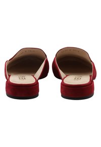 Rote Wildleder-Slipper mit flacher schwarzer Sohle, offenem Rücken und cremefarbener Innenauskleidung. Minimalistisches Design ohne sichtbare Beschläge.