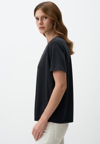 T-shirt nera a maniche corte realizzata in materiale morbido, con una vestibilità rilassata e scollo rotondo, abbinata a pantaloni chiari.