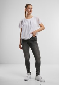 Blusa bianca a maniche corte con scollatura rotonda, abbinata a jeans skinny grigi e sneakers bianche. Tessuto morbido con vestibilità rilassata.