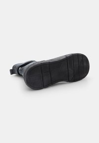 Botte noire mettant en avant une semelle en caoutchouc texturé avec des rainures verticales, un talon renforcé et un dessus lisse à l'arrière pour un soutien supplémentaire.