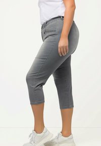Jean cropped gris en denim, présentant une coupe slim et une taille mi-haute. Associé à des baskets blanches pour un look décontracté.