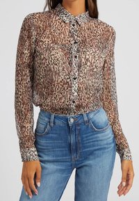 Kvinde iført gennemsigtig leopardprint skjorte med lange ærmer og knaplukning, stoppet ned i højtaljede blå jeans.