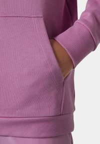 Sudadera rosa con un bolsillo frontal, puños acanalados y una textura suave. El diseño incluye un corte relajado y un acabado liso.