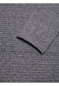 Grå stickad tröja i tyg med ribbade texturer, med en vikt cuff. Materialet verkar mjukt och något elastiskt.